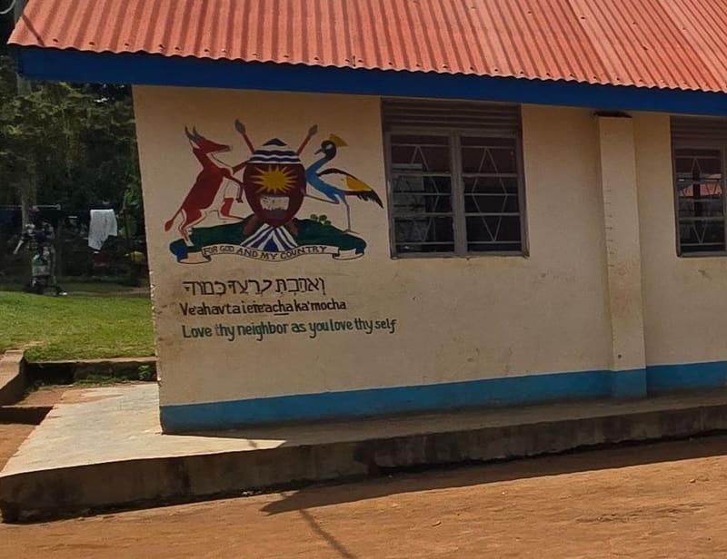 A wall mural of Uganda's coat of arms above the words "Love thy neighbor as you love thy self", written in Hebrew, transliteration and English.