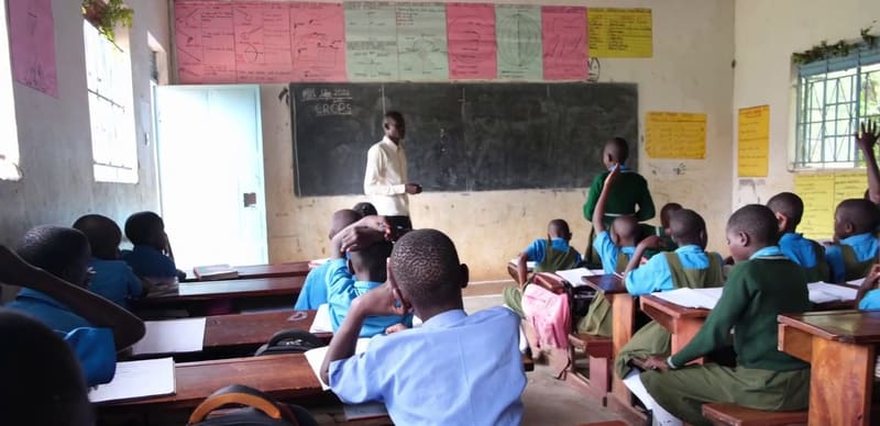 Students in a Hadassah classroom raise their hands while a teacher stands at the blackboard.