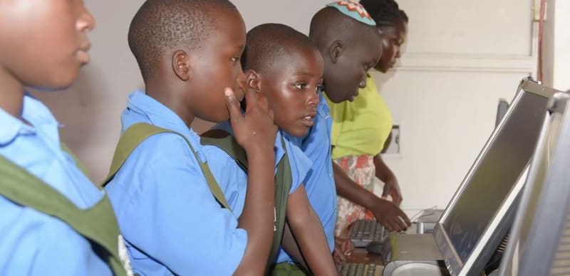 Hadassah pupils in blue uniforms, one wearing a kippah, gather at a computer with a teacher.