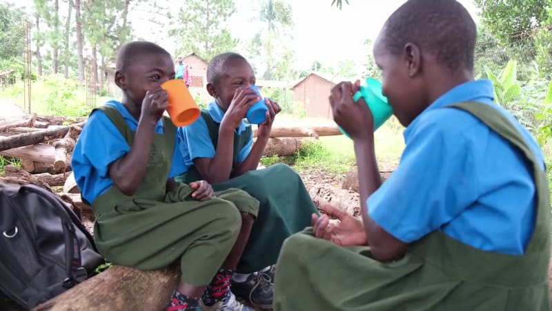 Hadassah pupils in blue shirts and green pinafores drink from colorful plastic cups.