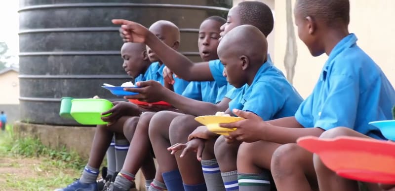 Hadassah students in blue uniforms eat from plastic plates, sitting side by side.