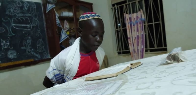 At Hadassah, a student wearing a kippah and a tallit reads from a book at a cloth-covered table.