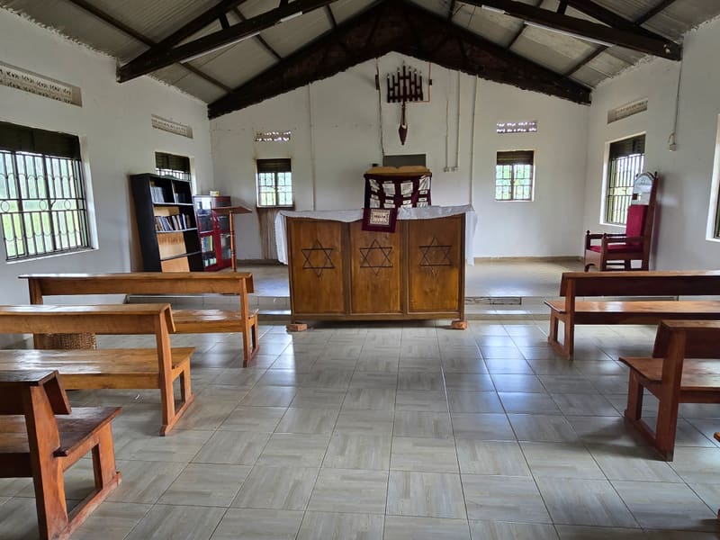 Inside a synagogue: wooden benches face an ark decorated with Stars of David, under a high beamed roof.